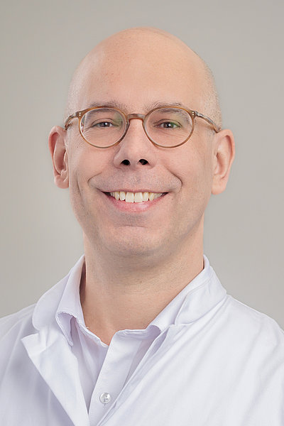 Porträt eines lächelnden Mannes mit Brille und weißem Hemd vor hellem Hintergrund
