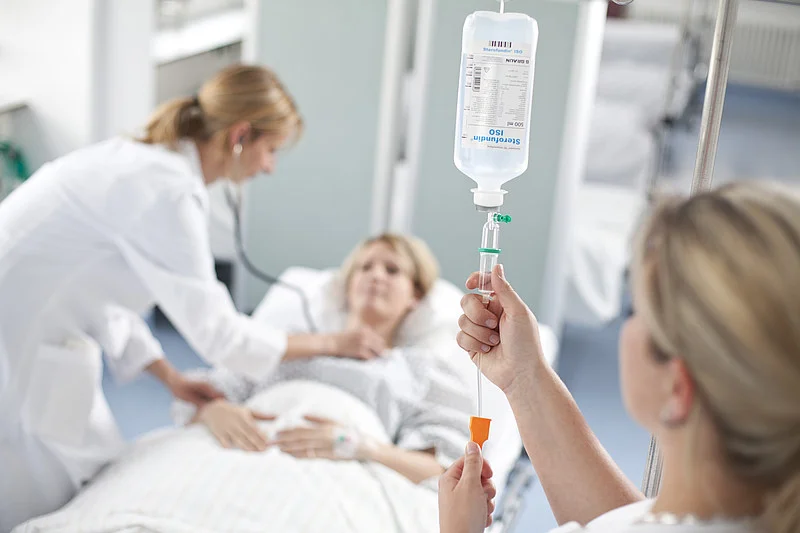 Krankenhauspersonal stellt Infusion an einem Patientenbett ein, Patient liegt auf der Liege
